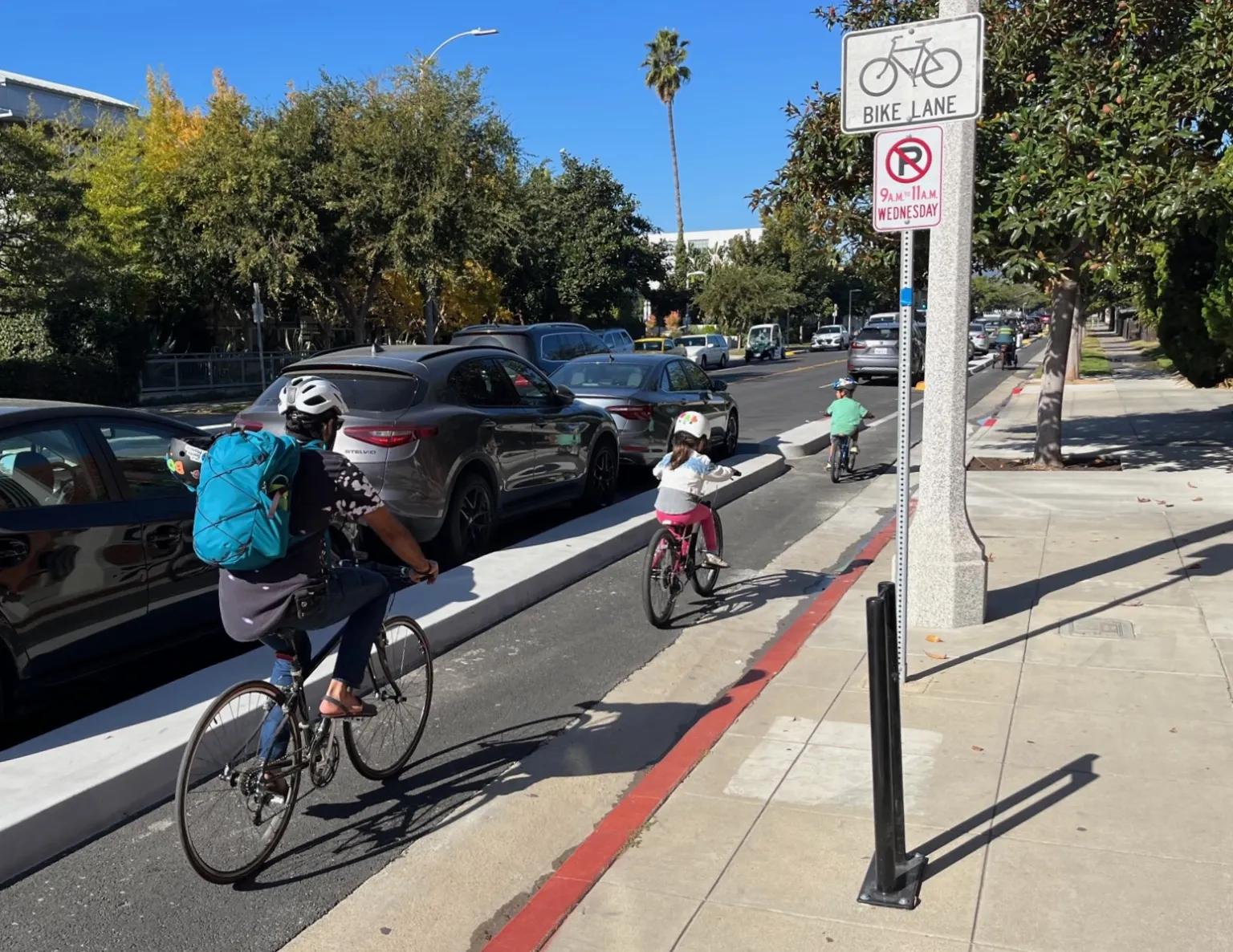 Protected bike lane (low concrete barriers) with two kids and an adult cycling